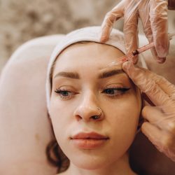 Portrait of young Caucasian woman getting botox cosmetic injection in forehead. Beautiful woman gets botox injection in her face.