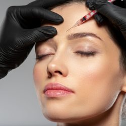 Young caucasian woman getting botox cosmetic injection in a forehead. Beautiful woman gets botox injection in her face. Adult girl gets cosmetic injection of botox in a clinic. Beauty treatments