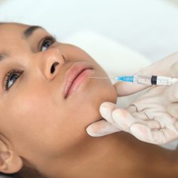 An african american lady at a spa, receiving a specialized aesthetic face treatment with a sharp focus on the precise technique used by the therapist