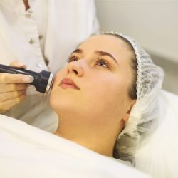 Unrecognizable crop cosmetician using modern machine for radiofrequency therapy on face of female client