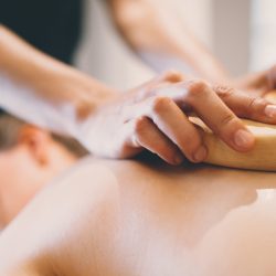 Massage therapist using wooden tool to massage patient in saloon