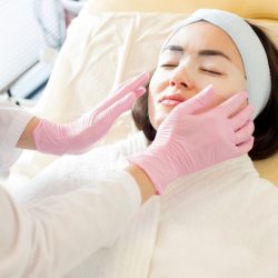 Portrait of unrecognizable cosmetologist applying refreshing eye mask to face of beautiful young woman performing beauty treatment